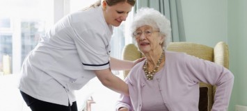 Health Care Assistant helping an elderly patient sit down in a comfortable chair.