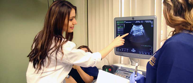 A young woman with long brown hair pointing at an ultrasound.