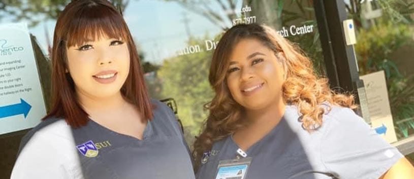 Two female SUI medical assisting students smile at the camera on a sunny day (outside of the school)